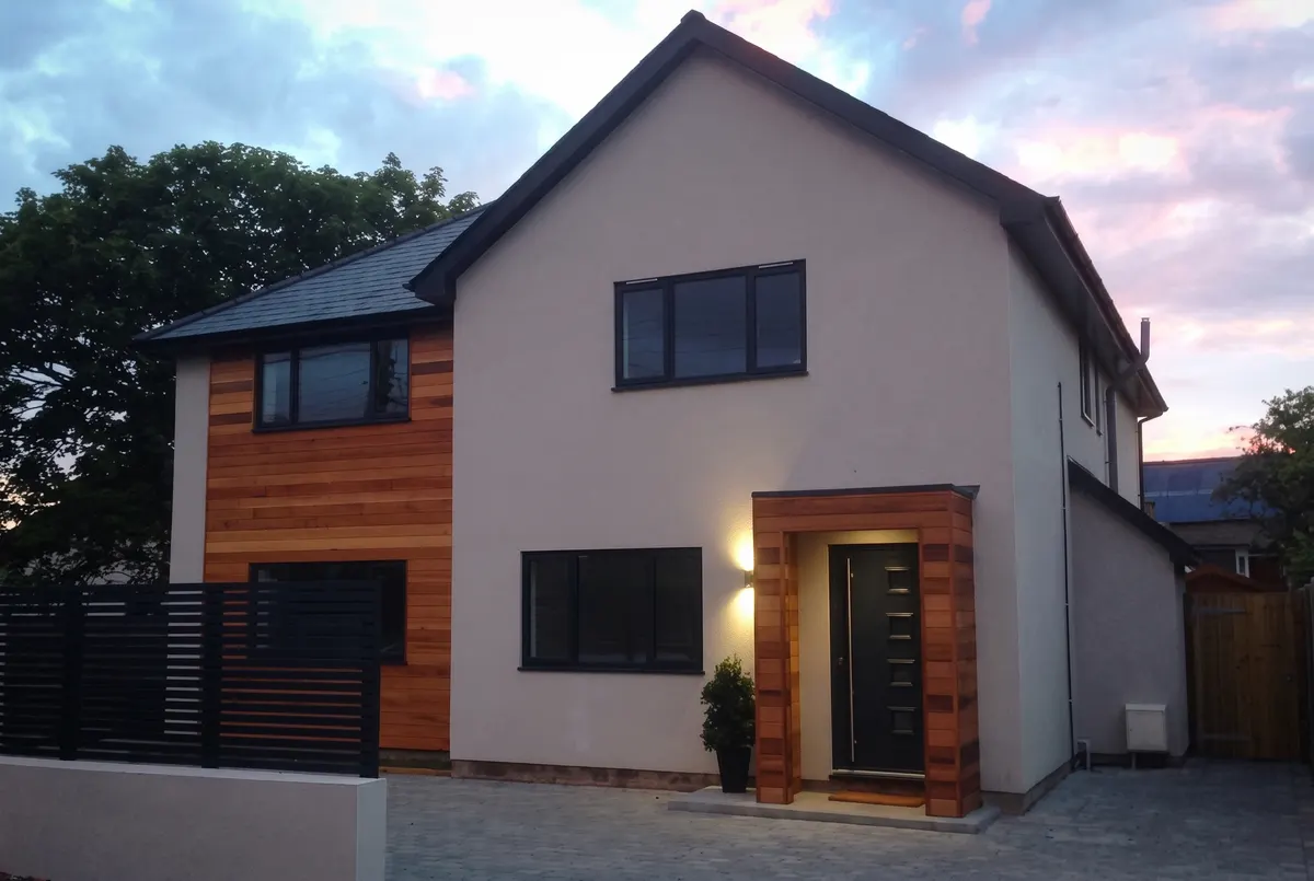 House extension and makeover with a rendered finish, cedar cladding panels and a timber framed porch at dusk