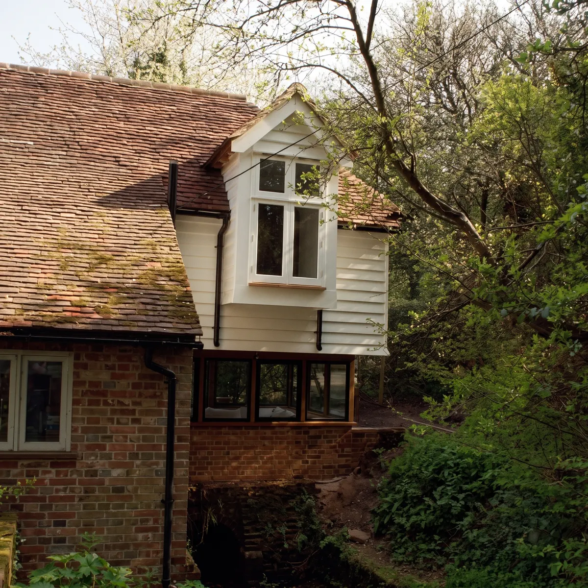 Weatherboarded extension built out over a mill stream on a listed mill house