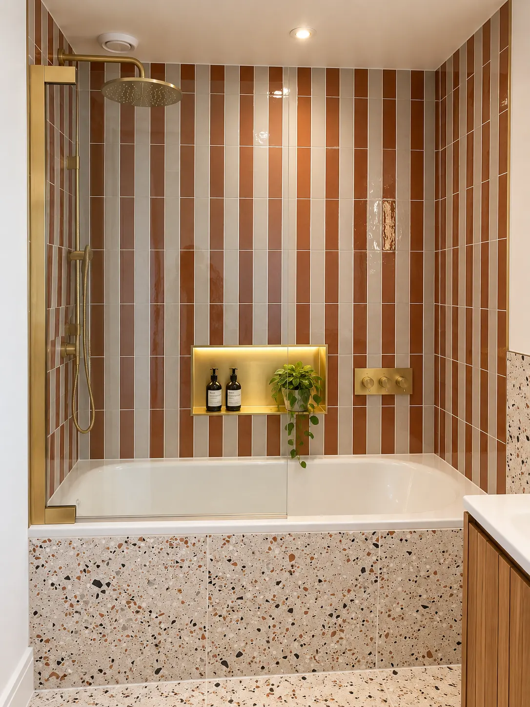 Bath with a terrazzo panel, brushed brass shower and a lit niche set into striped tiles