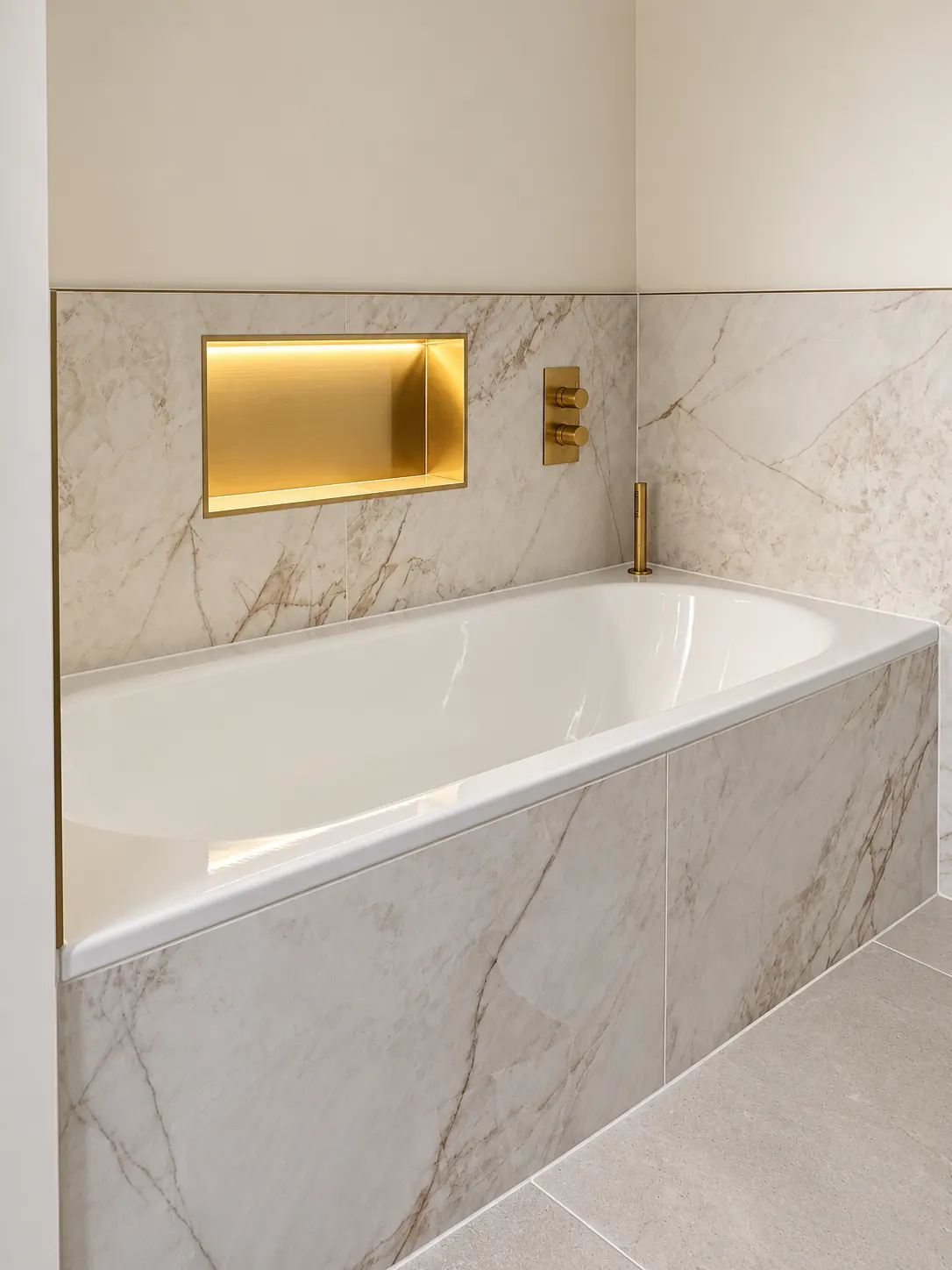 Built-in bath clad in marble effect porcelain with a brass filler and a lit brass niche